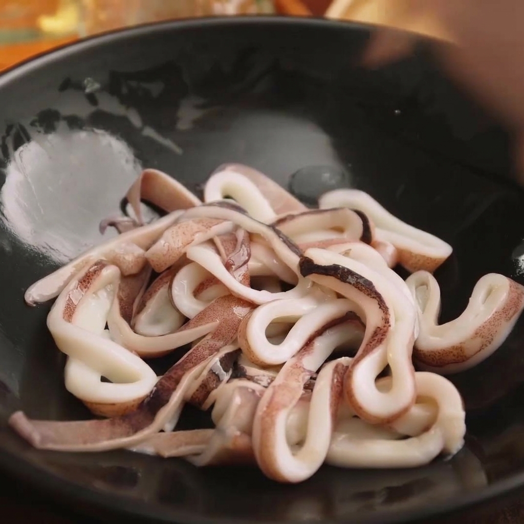黒いボウルに入れられた、下味をつける準備ができた新鮮なイカの輪切り。