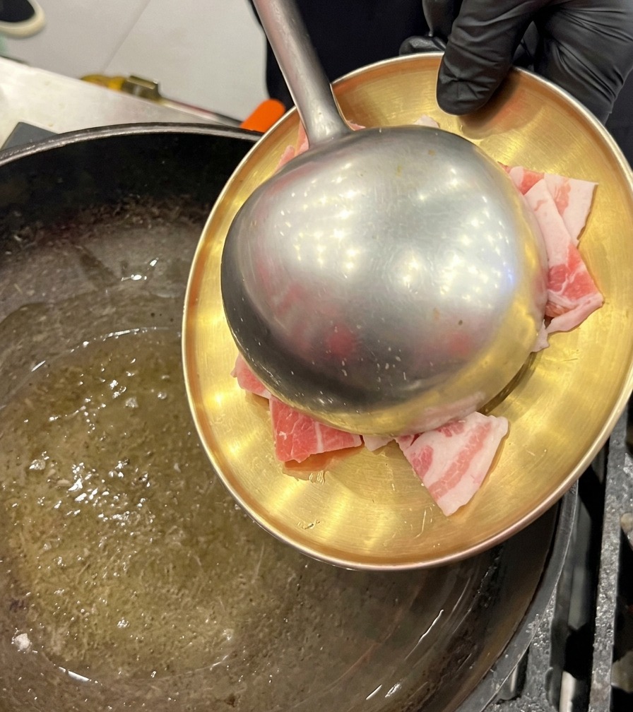 油を引いた中華鍋に、お皿から生の豚バラ肉のスライスを移して炒めている様子。