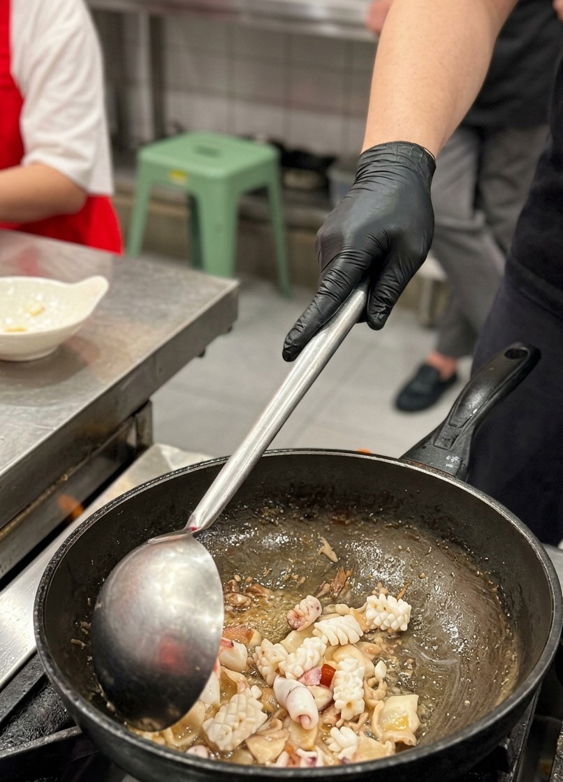 中華鍋の中で、香ばしく炒めた豚バラ肉と一緒に、格子状の切れ目が入ったイカを炒め合わせているクローズアップ写真。
