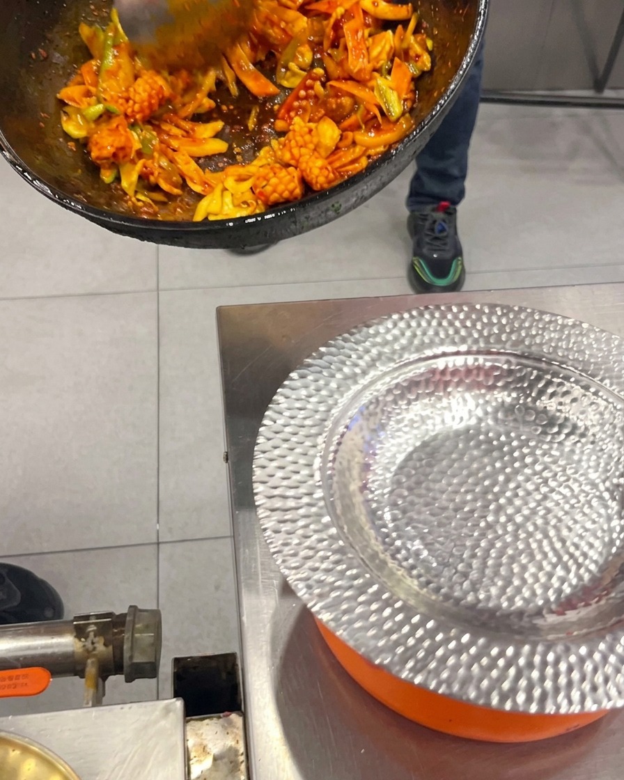 中華鍋から、炒め上がった韓国風のイカと豚バラ肉のピリ辛炒めを銀色のお皿に盛り付けている様子。
