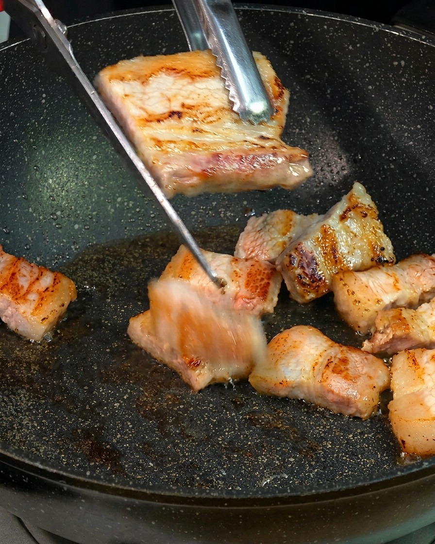 フライパンの上で、こんがり焼けた豚バラ肉をキッチンバサミで一口大にカットしている様子