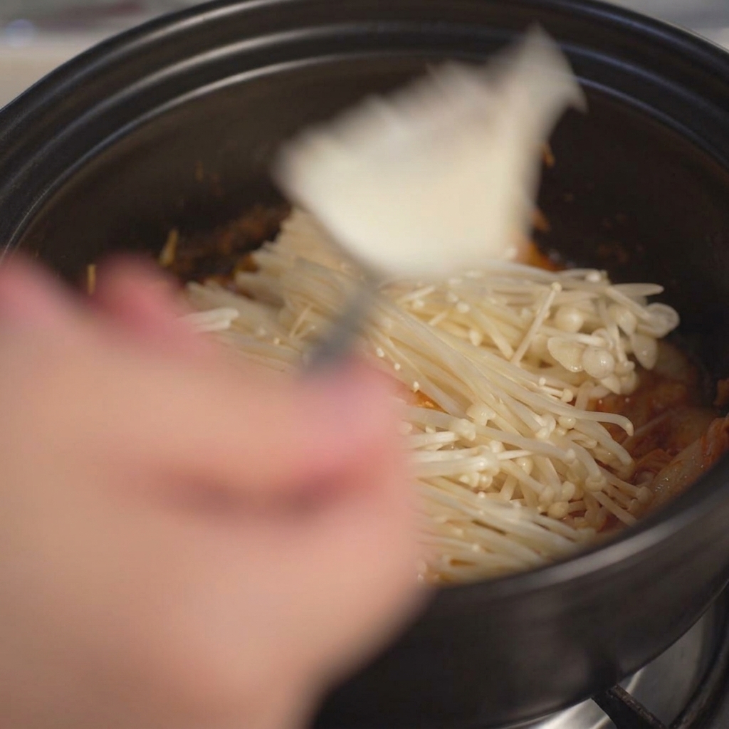 スプーンを使って、大きめにすくった白い豆腐を土鍋の中に投入している様子。