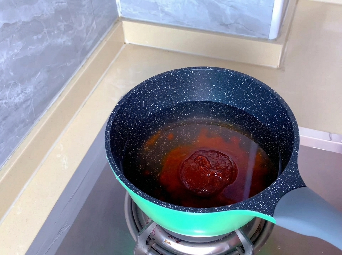 鍋に入った透明な水の中に、赤オレンジ色のキムチスープの素が沈んでいる様子。