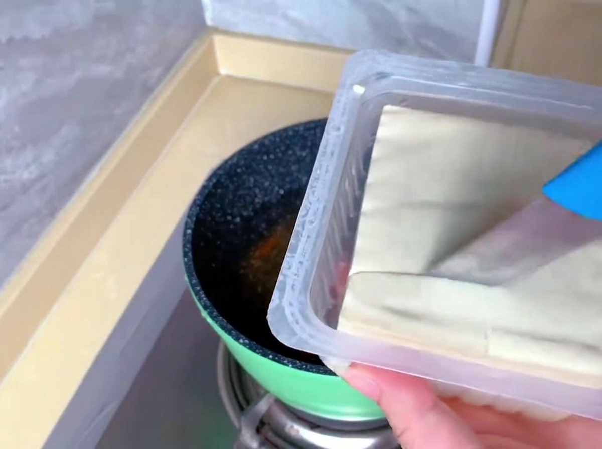 青い柄のナイフを使い、プラスチックのパックに入ったままの白い絹ごし豆腐をカットしている手元。