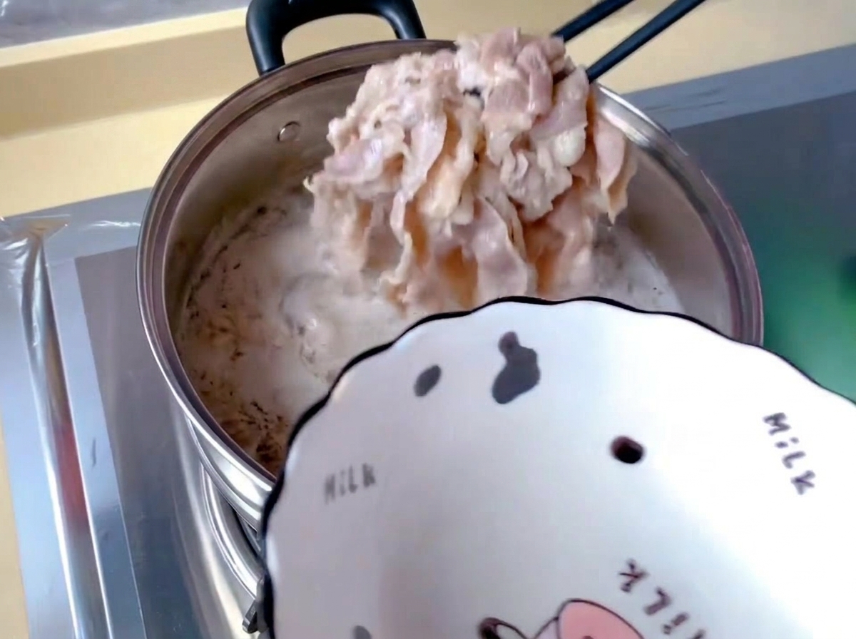 白いアクと泡が浮いた沸騰したお湯から、黒い箸を使って薄切りの牛肉を引き上げている様子。