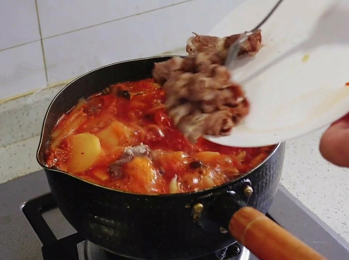 煮立つキムチチゲの鍋に、白いお皿から下茹でしておいた牛バラ肉を戻し入れている様子。