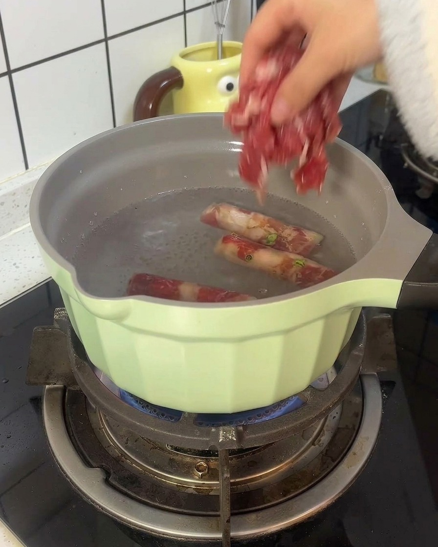 薄緑色の鍋の熱湯で牛薄切り肉を下茹でしている様子。