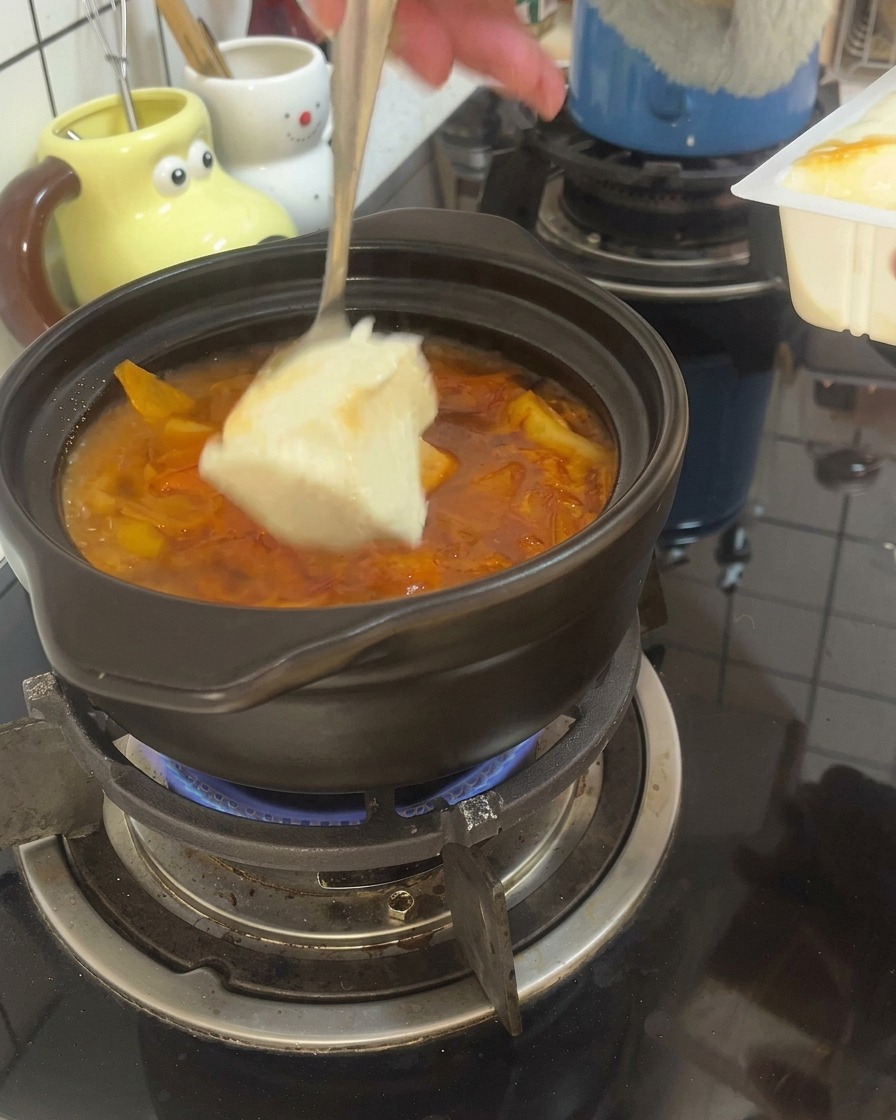 スプーンで大きくすくった絹ごし豆腐を、土鍋でグツグツ煮立つ赤いスープの中に入れている様子。