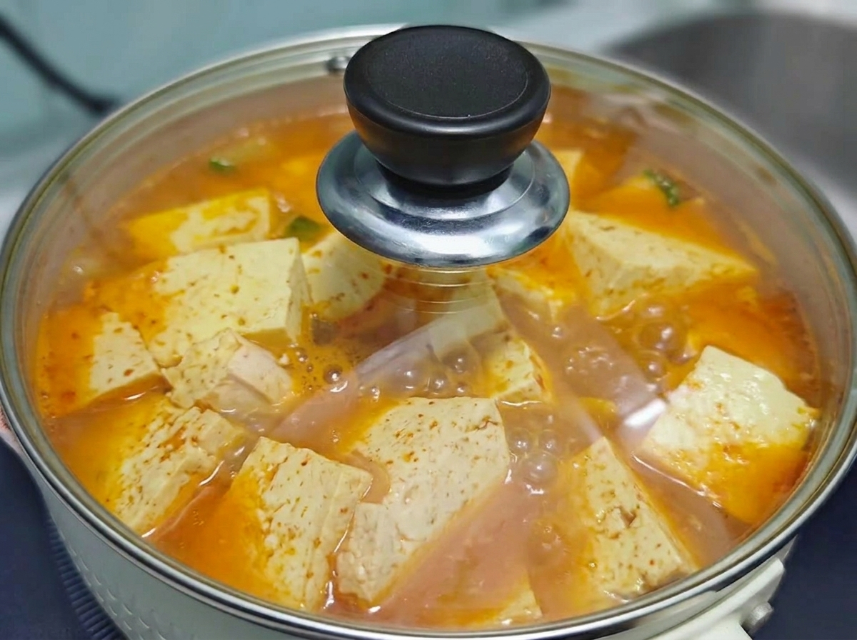 コンロの上でグツグツと沸騰する、韓国風の牛肉豆腐キムチスープの鍋に、透明なガラス蓋がされている様子。