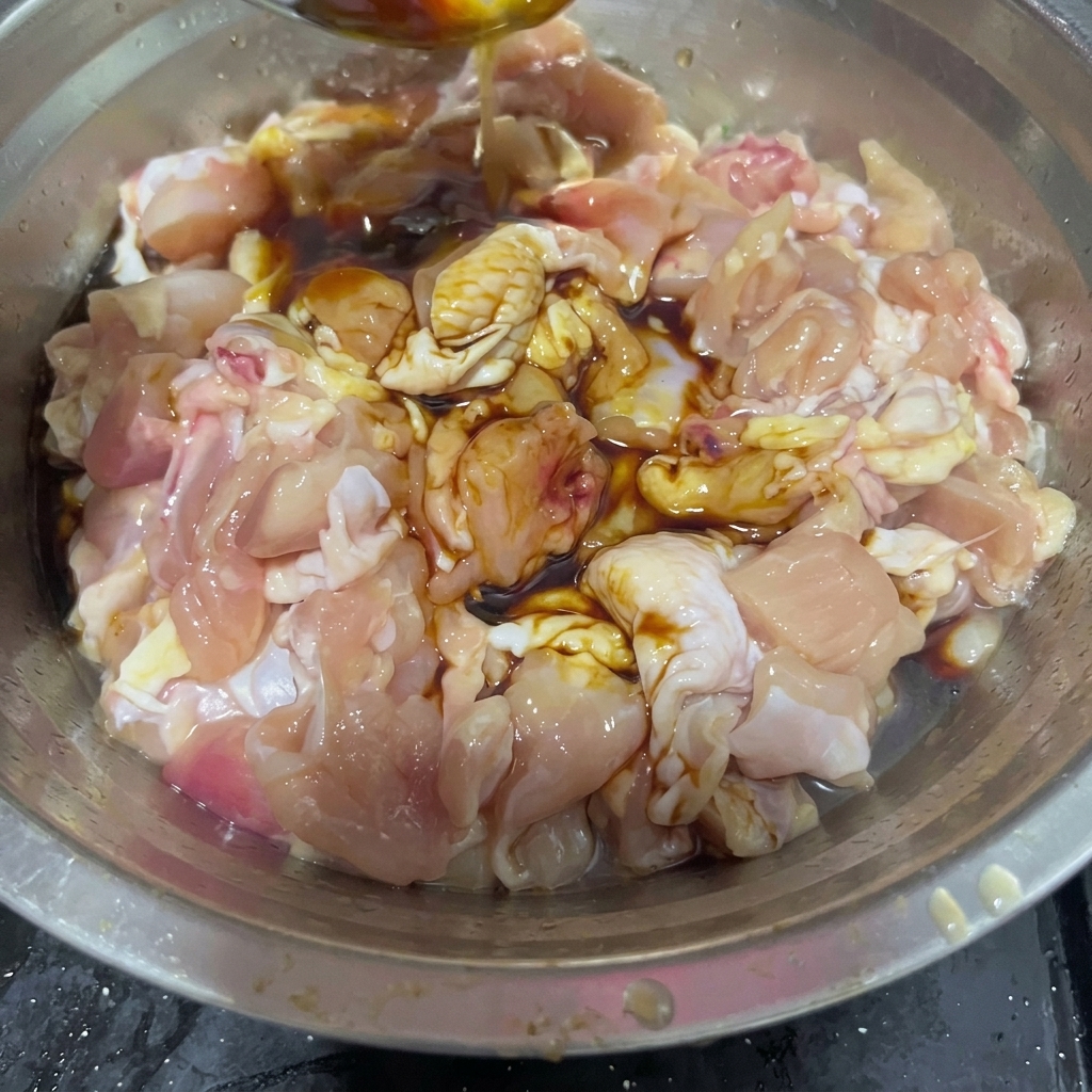 ステンレス製のスプーンから、生の鶏肉と濃い色の調味料が入ったボウルに料理酒が注がれている様子。