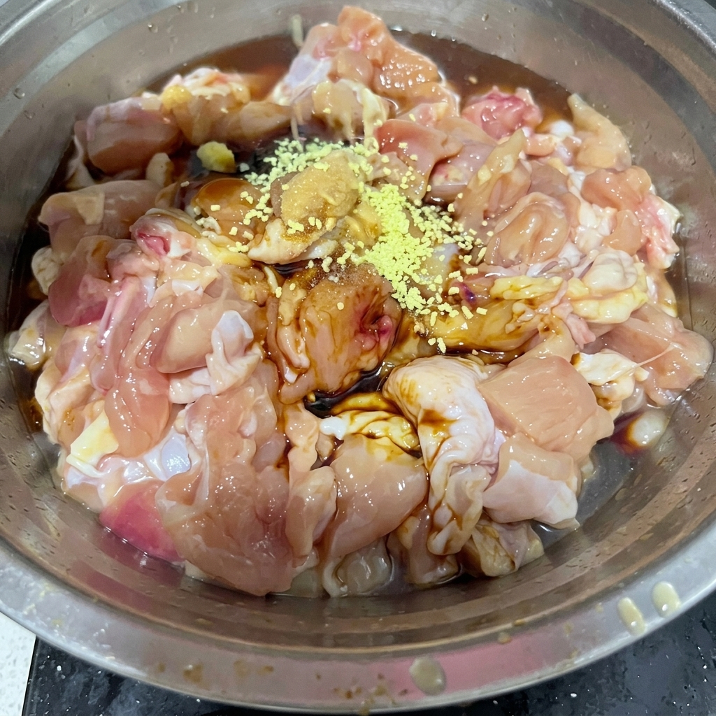 金属製のボウルに入った生の鶏肉の上に、黄みがかった鶏ガラスープの素と白い塩が振られている様子。