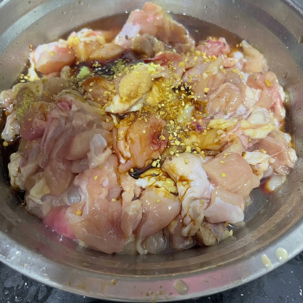 ステンレス製のミキシングボウルの中で、タレに漬かった鶏肉の上に乾燥したバーベキューシーズニングミックスが振りかけられている様子。