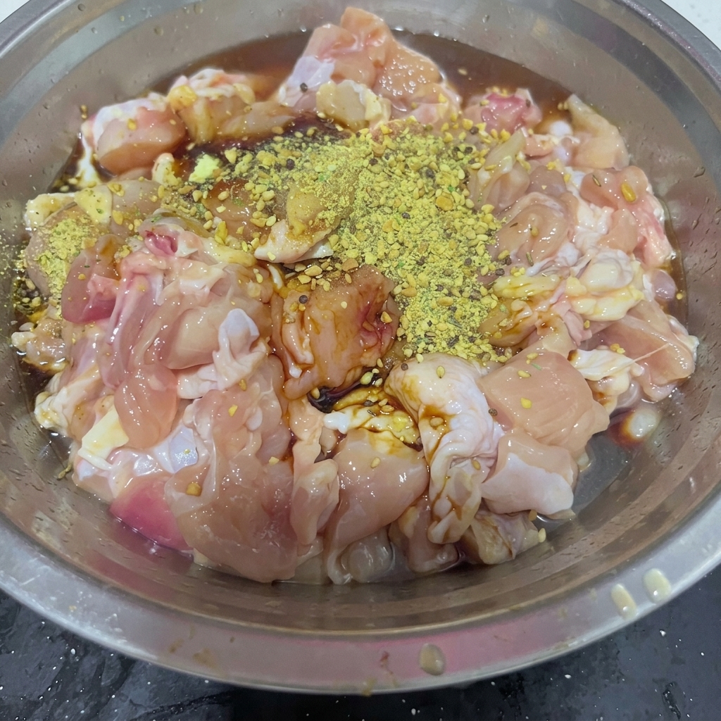 ステンレス製のボウルに入った、味付けされた鶏もも肉の上に白砂糖が振られている様子。