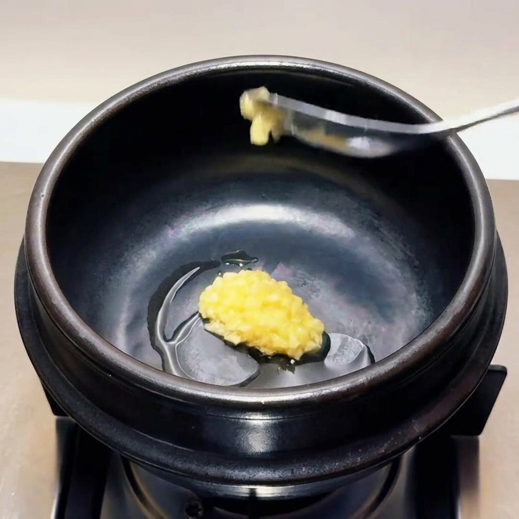 温まった土鍋の中のごま油に、スプーンいっぱいの刻みニンニクを入れている様子。