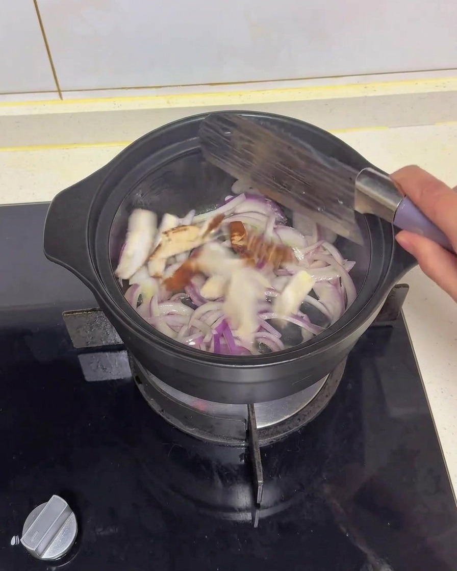 黒い鍋の中で、しんなりし始めた赤玉ねぎとスライスした椎茸をスパチュラで炒め合わせる様子。