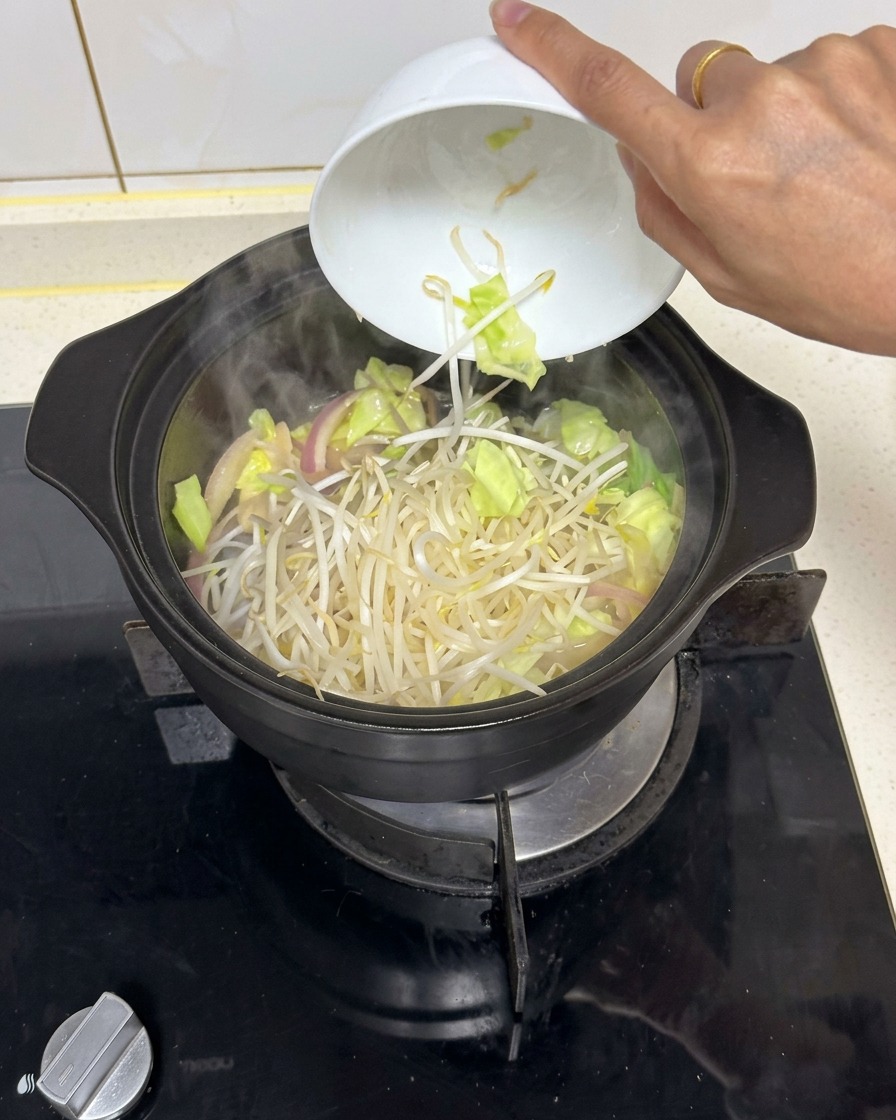 炒めた野菜が入った黒い鍋に、白い陶器のボウルから新鮮なもやしをドサッと加える様子。
