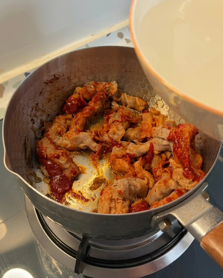 味付けした牛肉が入った鍋に、白いボウルから白濁した米のとぎ汁を注いでいる様子。