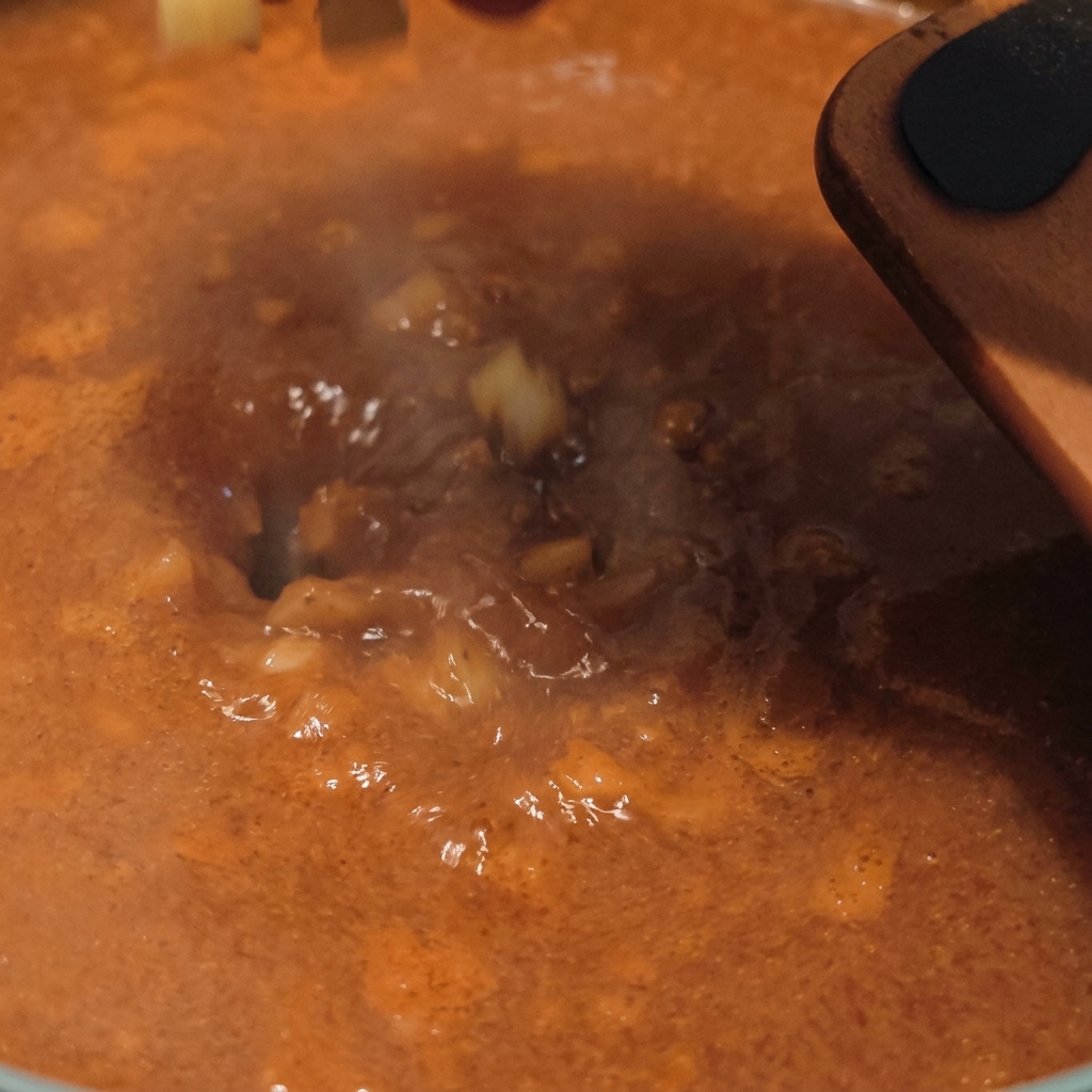 湯気が立ち上るオレンジ色のチゲスープの中に、角切りにした生のじゃがいもを投入している瞬間。