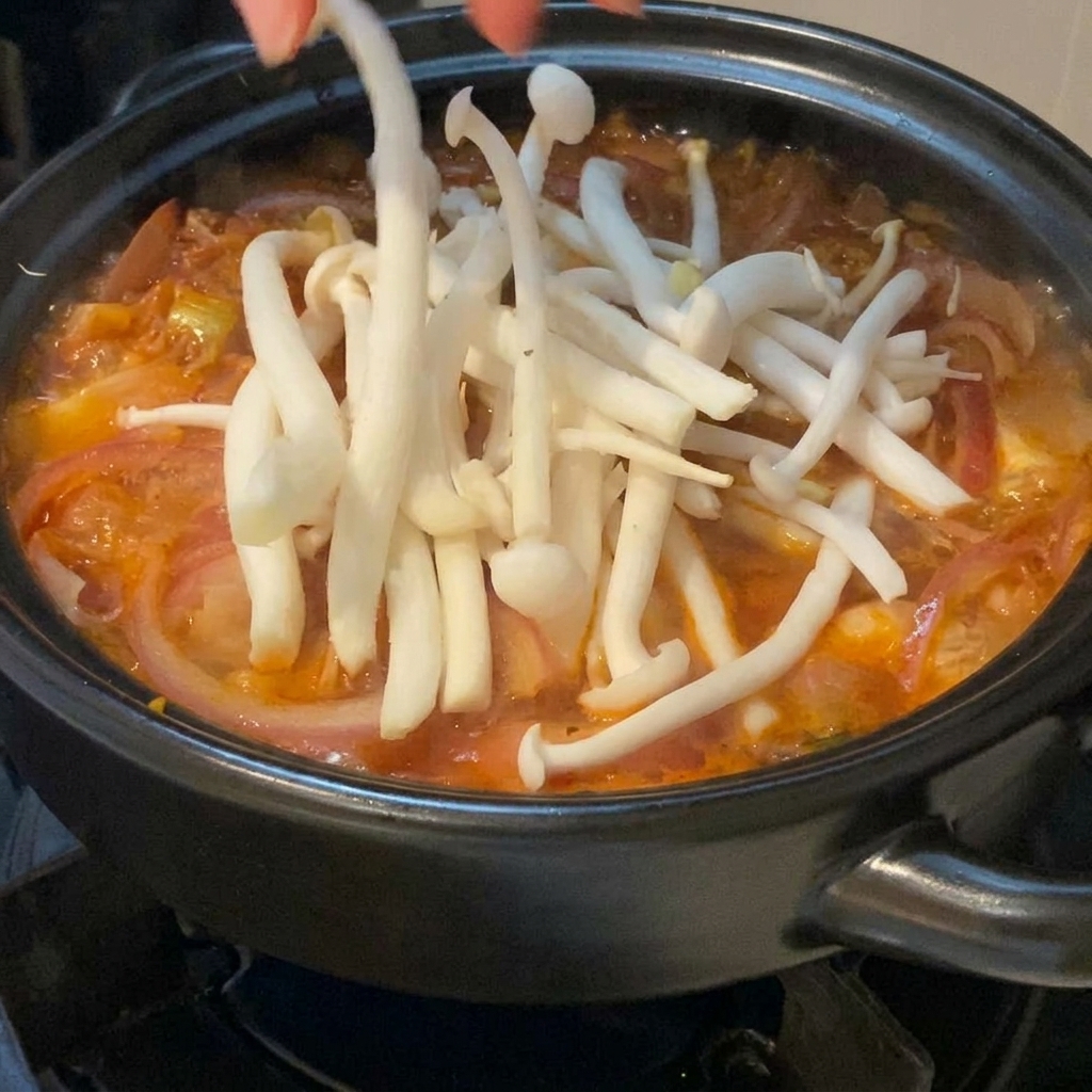 黒い土鍋で沸騰する真っ赤なキムチスープの上に、手で丁寧に並べられている新鮮な白いブナピー。