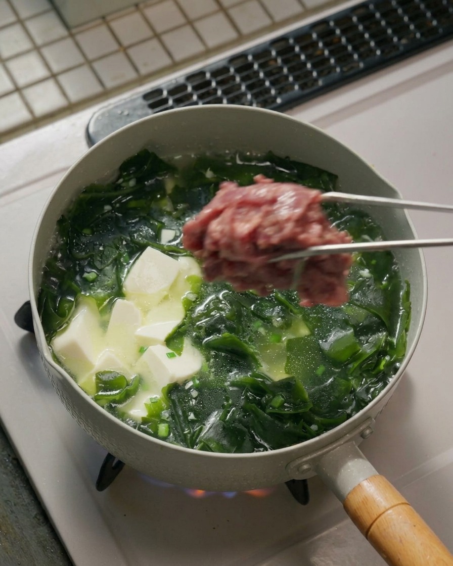 トングで下味をつけた牛肉を鍋に入れて広げている様子。