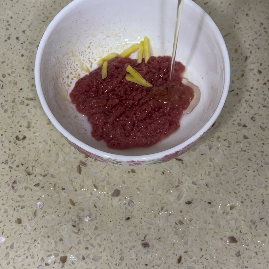 白いボウルに入った牛ひき肉に、生姜の薄切りを乗せ、調理油を回しかけている様子。