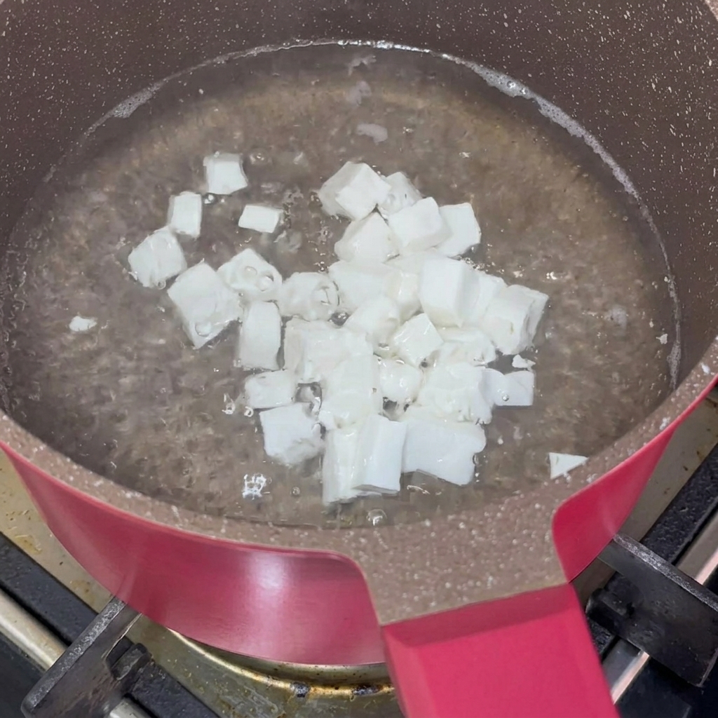 ピンクの鍋でサイコロ状の絹ごし豆腐が茹でられている様子。