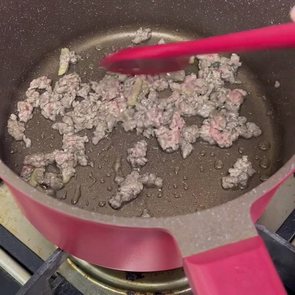 鍋で赤色のヘラを使ってひき肉を炒めている様子。