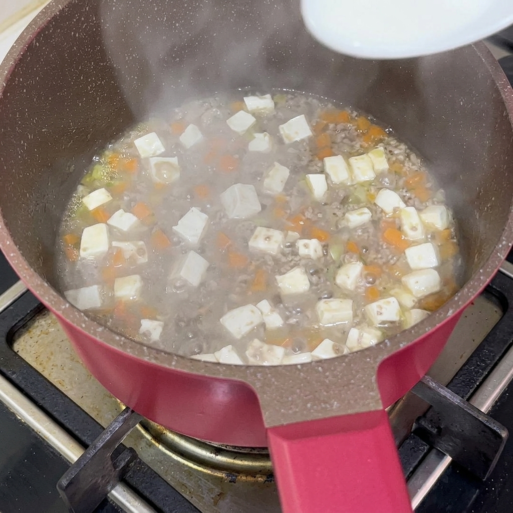 スプーンで水溶き片栗粉を煮込み鍋へ加えている様子。