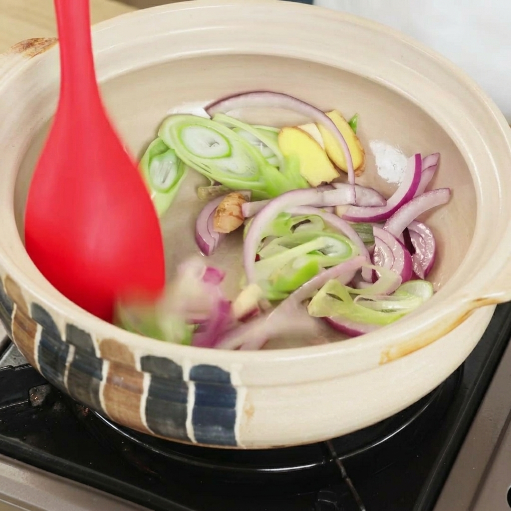 赤いヘラで香味野菜を炒めている様子。