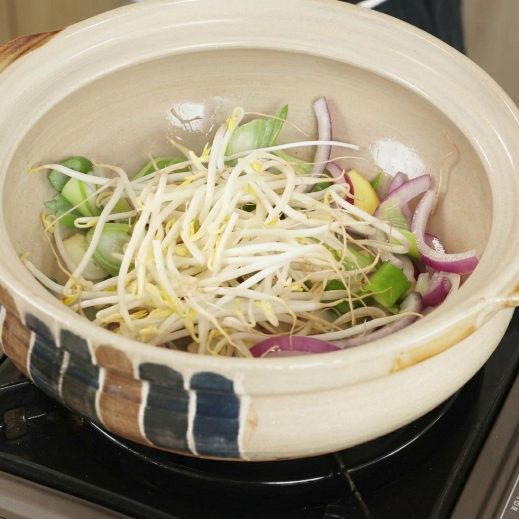 炒めた香味野菜の上にもやしを乗せる様子。