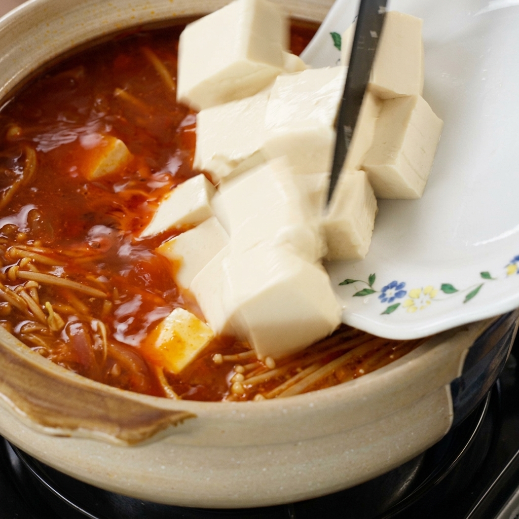 豆腐とえのきを鍋に入れる様子。