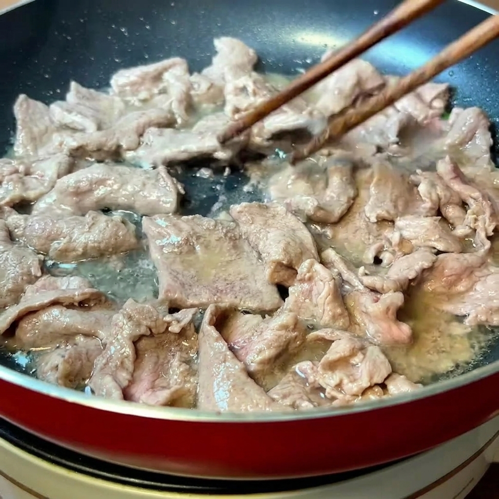 熱したフライパンで、菜箸を使って牛肉を素早く炒めている様子。