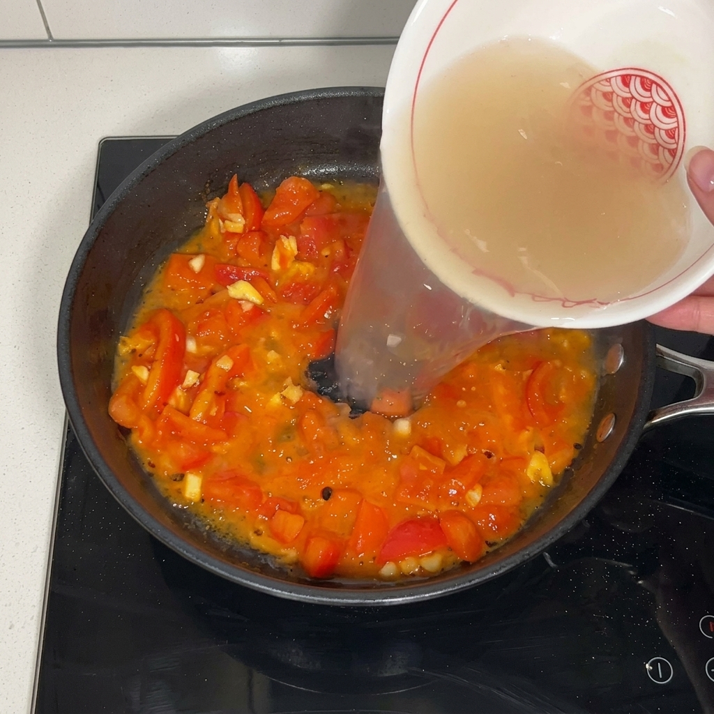 トマトを炒めたフライパンに、先ほどの牛肉の茹で汁を注ぎ入れている様子。