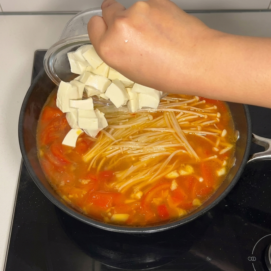 角切りにしたソフト豆腐を、静かにスープの鍋へ入れている様子。