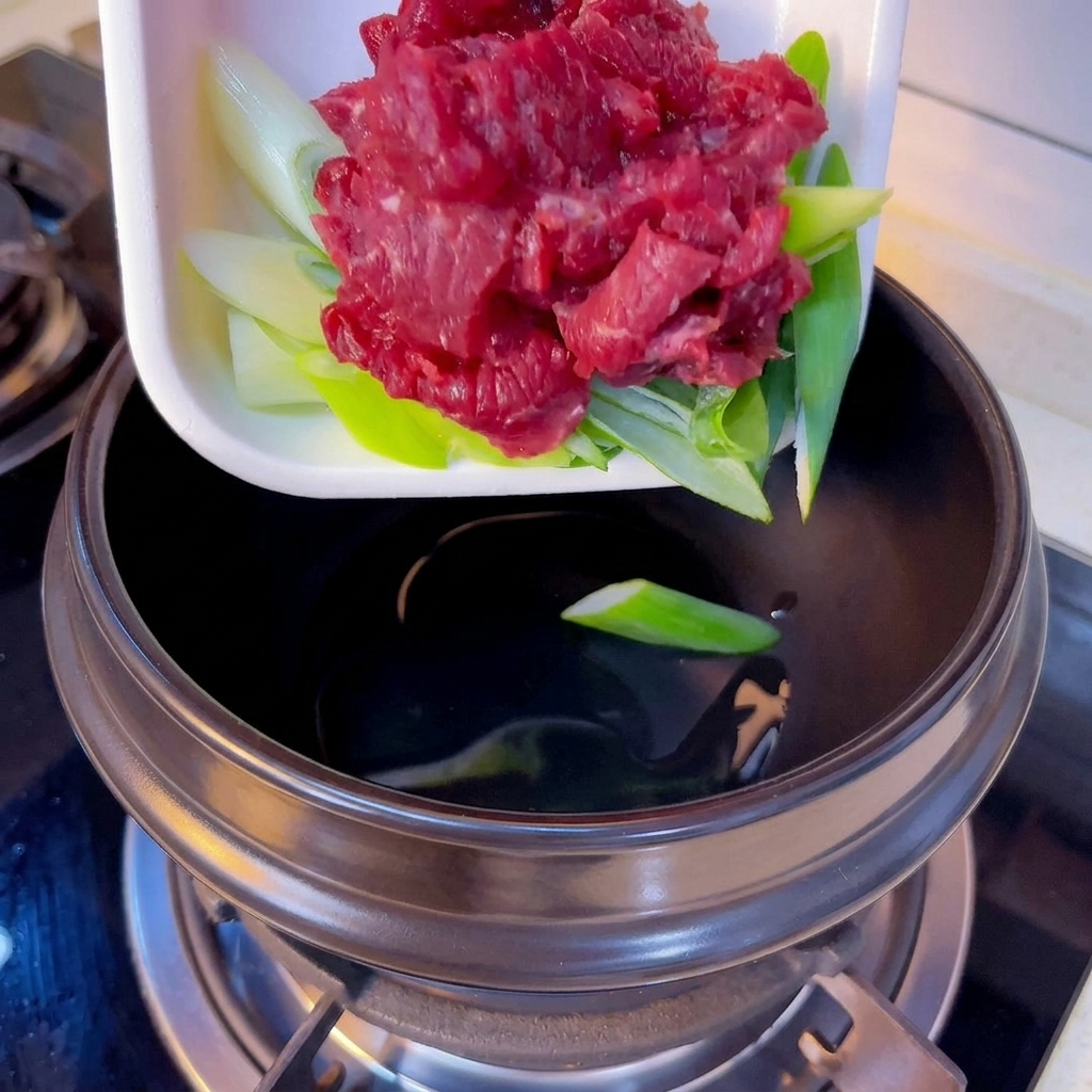 熱した土鍋に、牛肉の薄切りと刻んだ長ねぎを入れる様子。