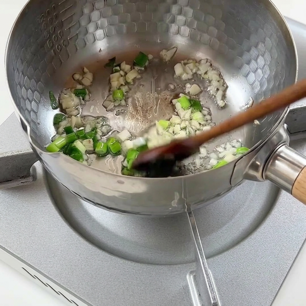 鍋で刻んだネギとニンニクを炒めている様子