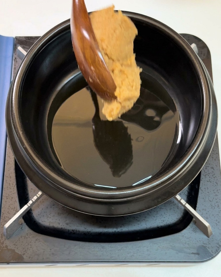 ごま油を熱した黒い鍋に、木べらでたっぷりのテンジャンを加えている様子。