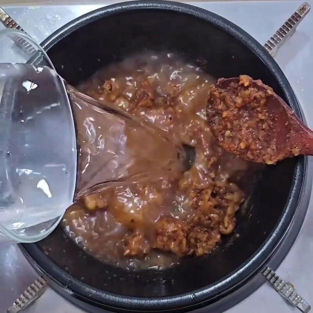 ガラス容器から透明な水を、ジューシーな豚肉と味噌の入った鍋に注いでいる様子。