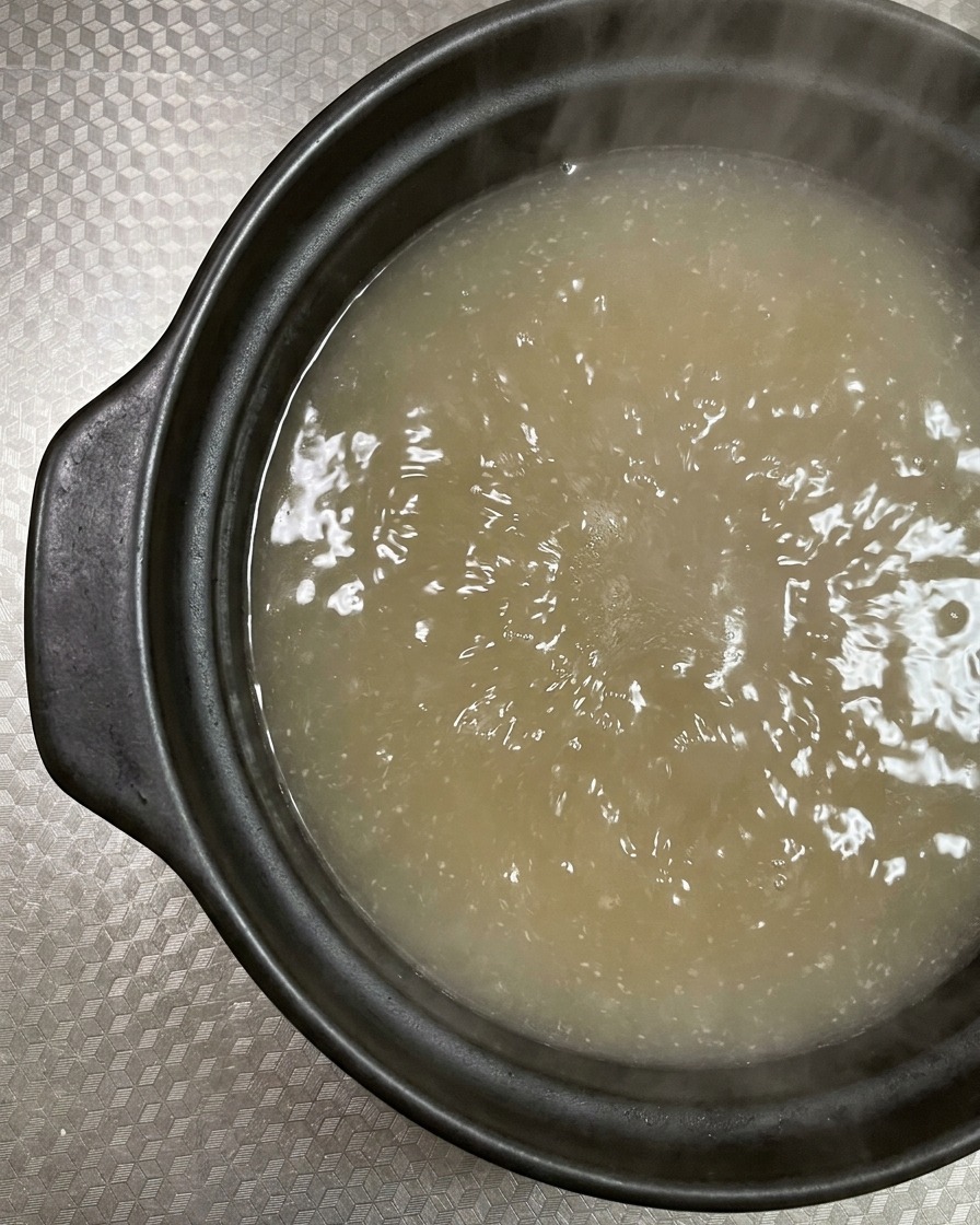 グツグツ煮立つ土鍋のスープに、脂ののった生の豚バラ薄切り肉を入れている様子。