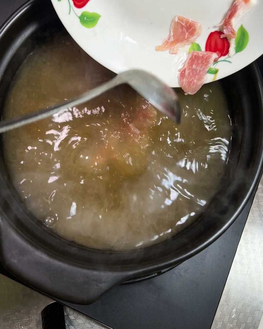 煮立っているスープに、鮮やかなオレンジ色のにんじんと薄黄色のじゃがいもを加えている様子。