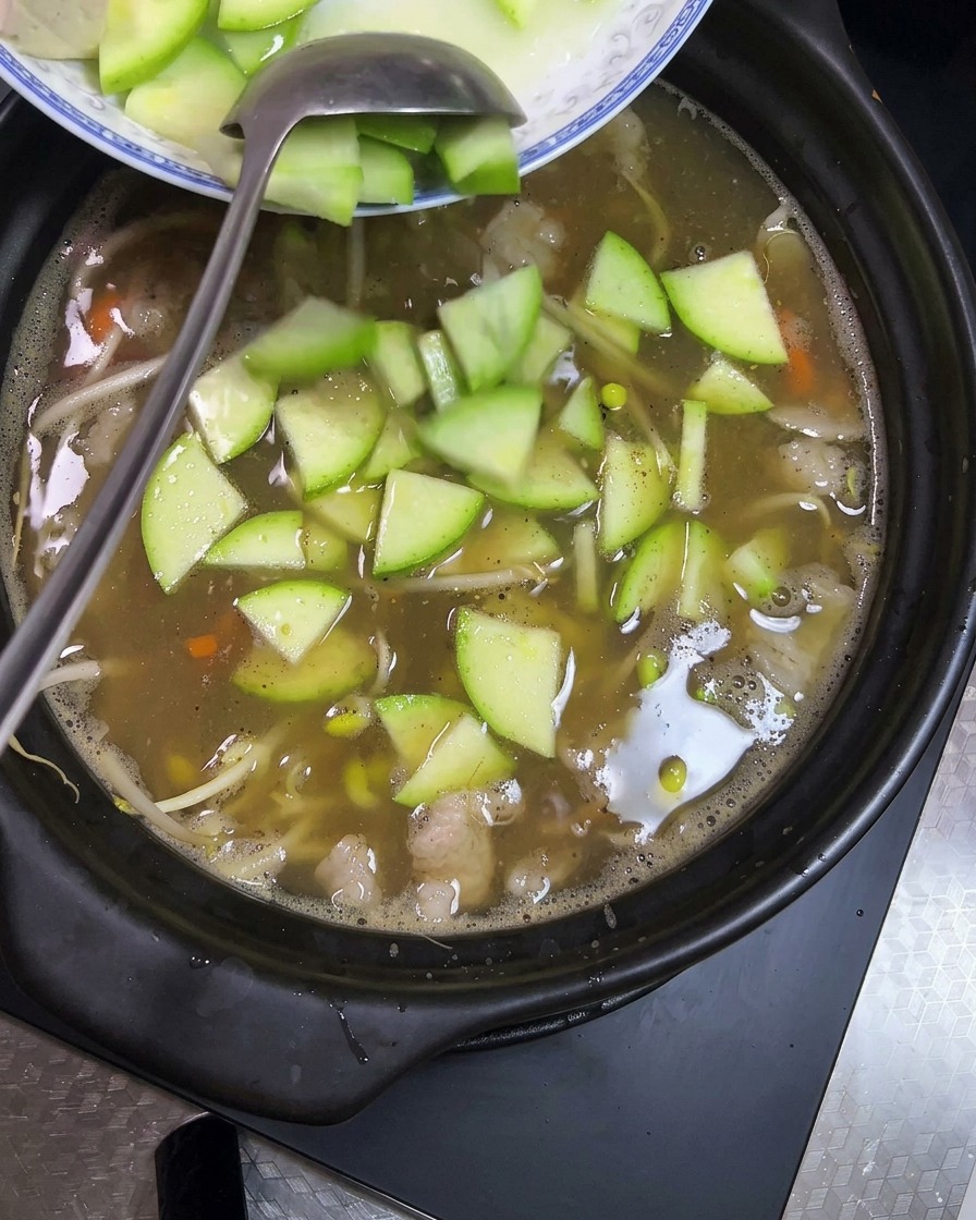 グツグツ煮立つ土鍋に、角切りの豆腐とスライスした緑色のズッキーニを加えている様子。