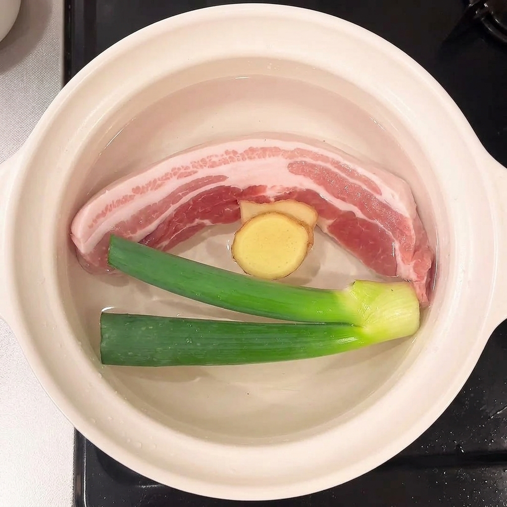 豚バラ肉と一緒に鍋に浮かぶ長ネギと生姜の薄切り。