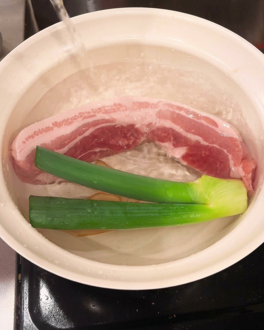 豚肉と香味野菜が入った鍋に料理酒を注ぐ様子。