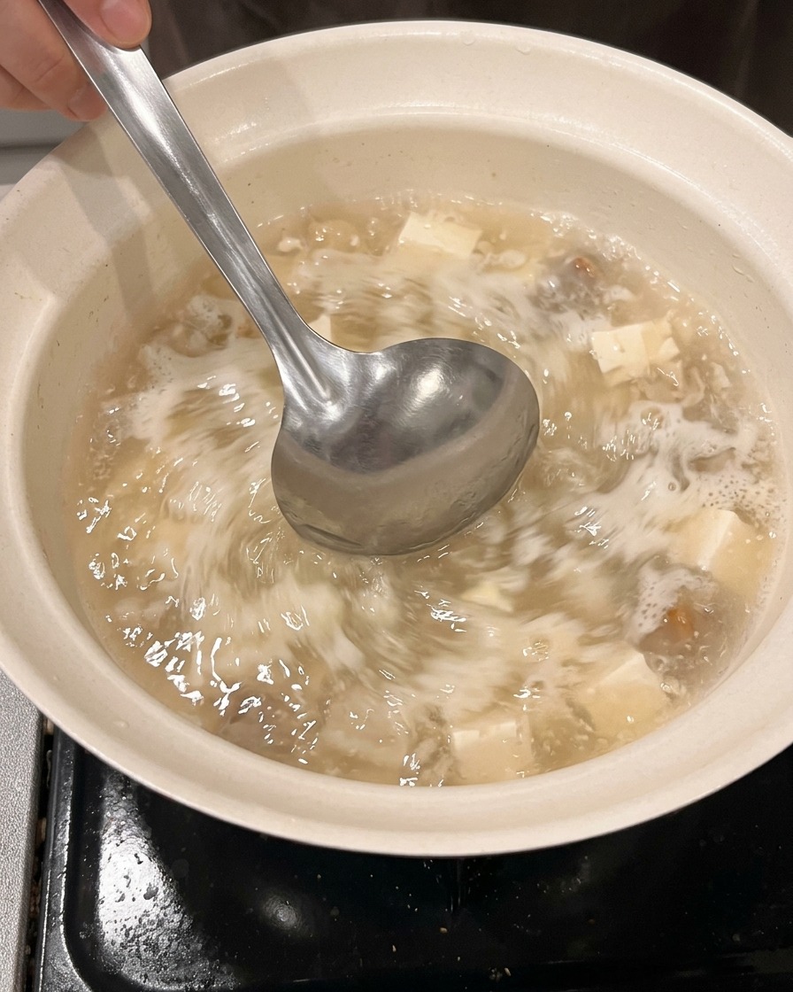 きれいな鍋に計量カップから水と酒を注いでいる様子。