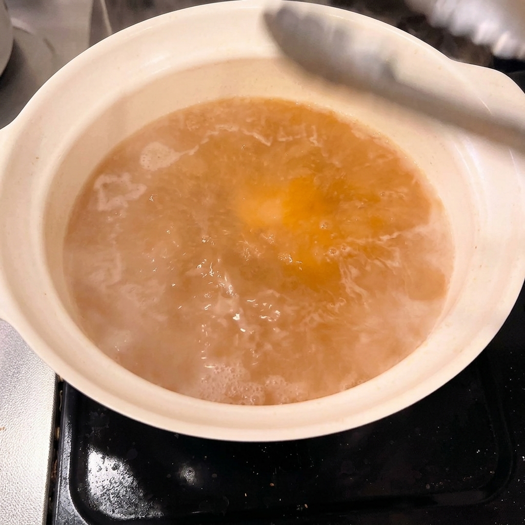 調味料を合わせた煮汁の入った鍋に、厚切りの豚バラ肉をトングで並べ入れている様子。