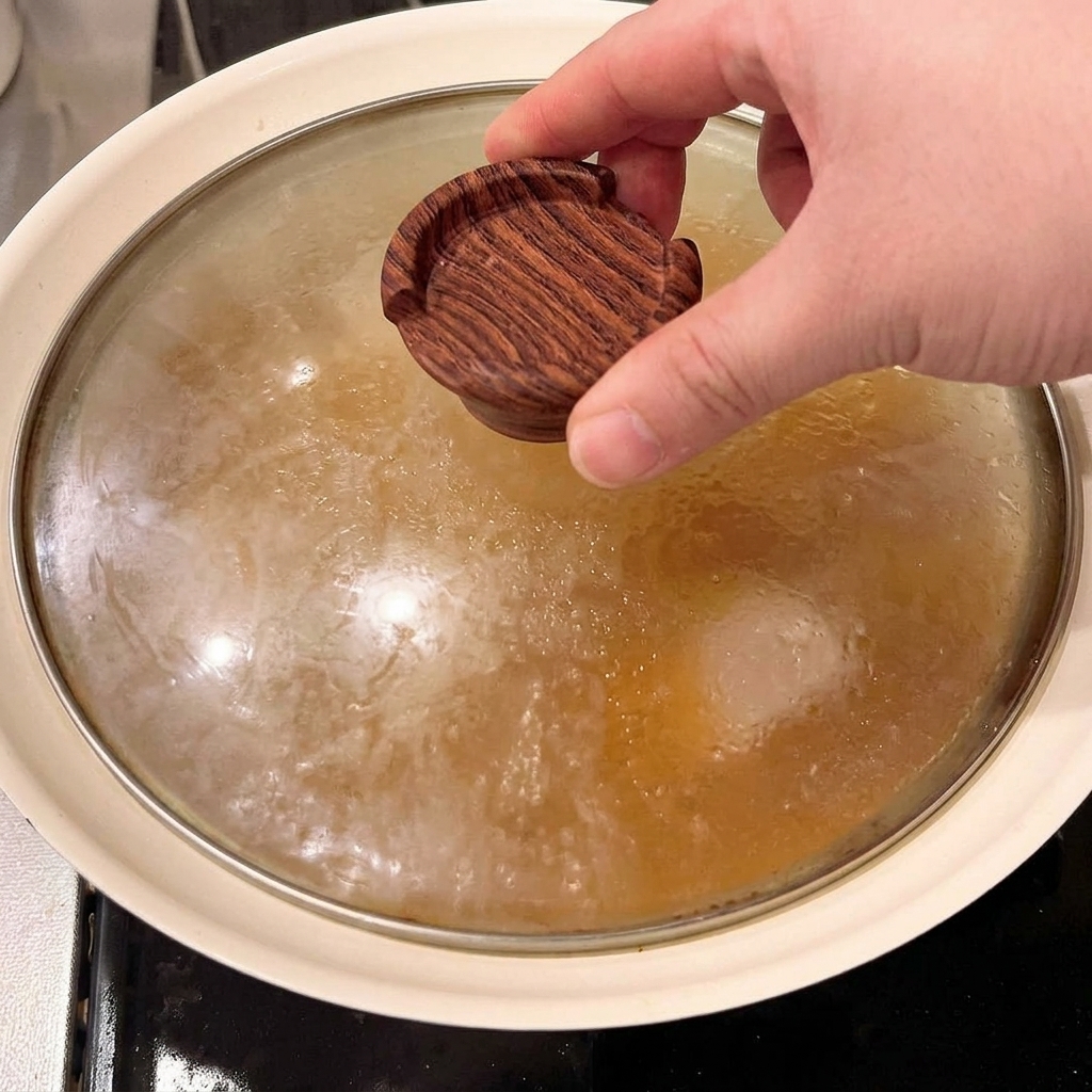 煮立っている煮汁と豚バラ肉の上に、木製の落とし蓋を被せているところ。