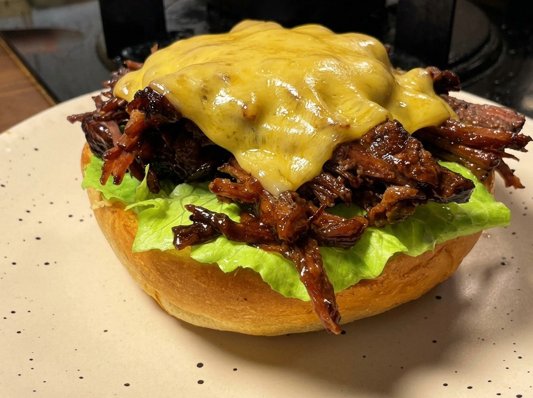 プルドビーフバーガーの上にのせたスライスチーズを、ハンドルトーチ（バーナー）で香ばしく炙って溶かしている様子。