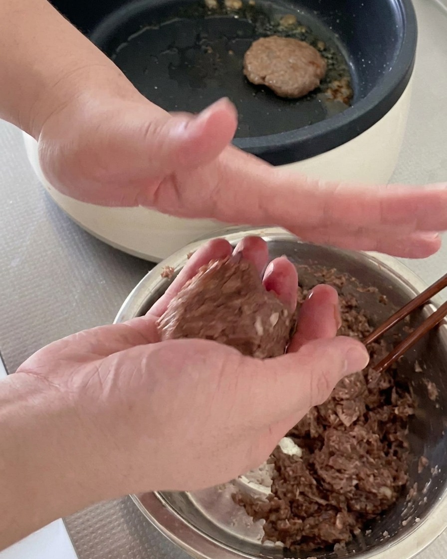 両手を使って牛ひき肉を丸め、ハンバーガーのパティの形に整えている様子