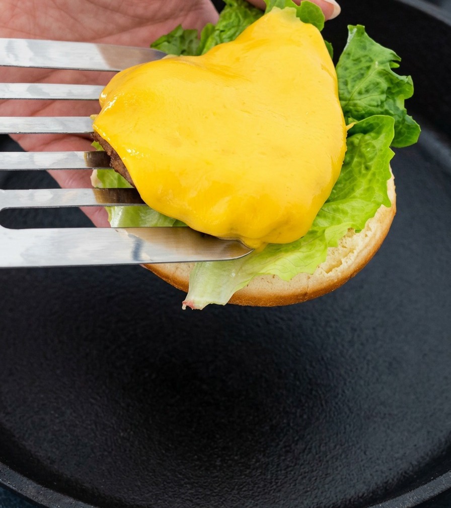 チーズがとろけたビーフパティをフライ返しですくい、バンズの上にのせている様子