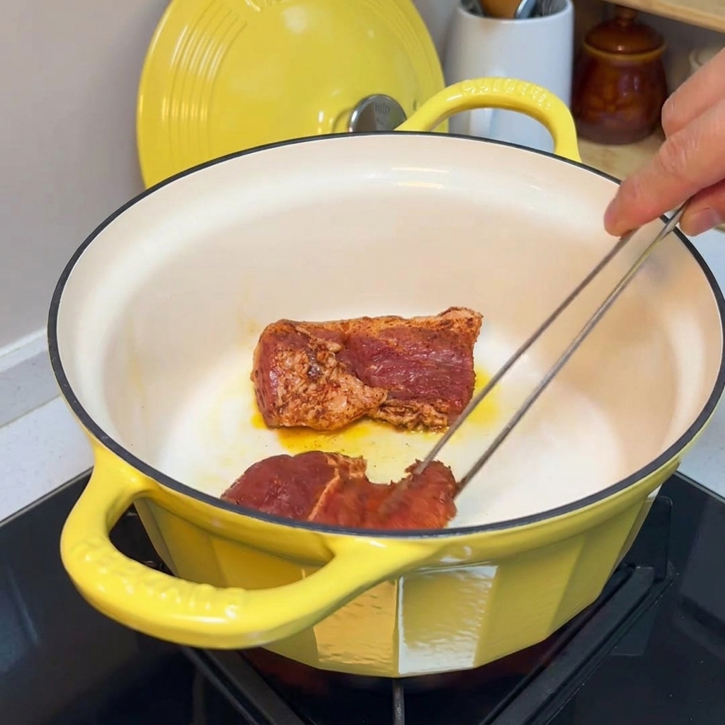 黄色い鋳物鍋で、下味をつけた豚肉の表面を焼き付けている様子。